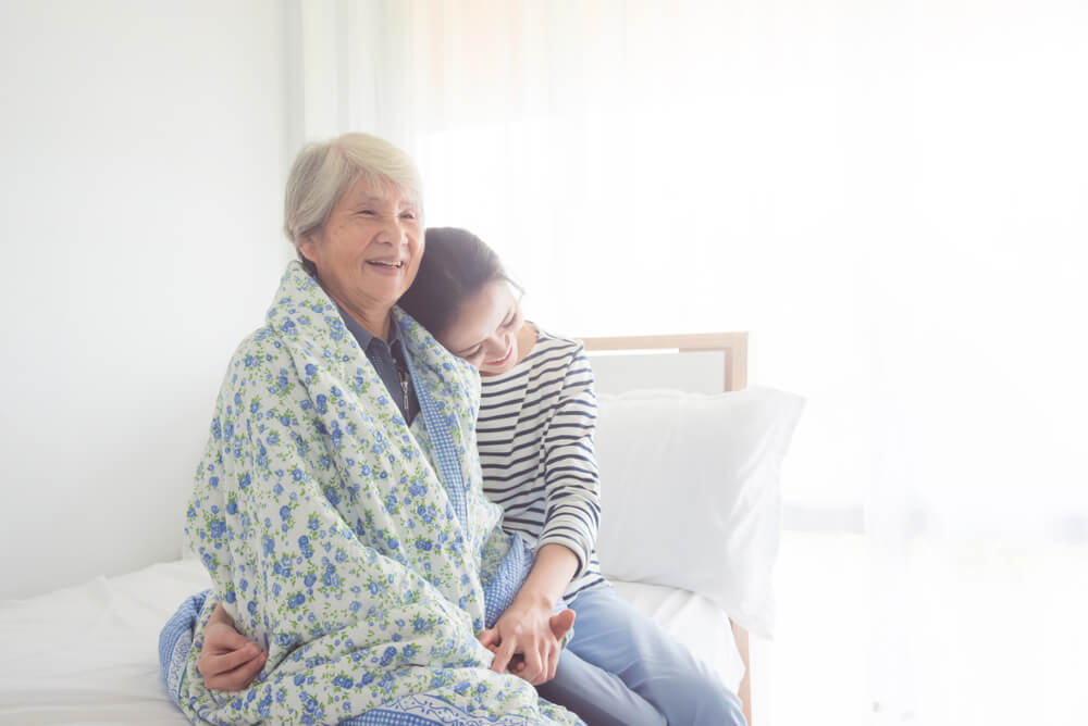 A daughter resting her head one her elderly mother's shoulder. 